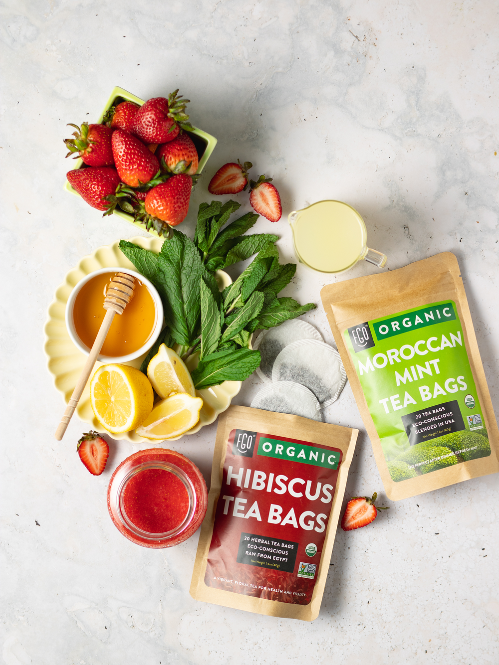 Raw ingredients for hibiscus mint tea: honey, fresh strawberries, lemon wedges, mint leaves for garnish.