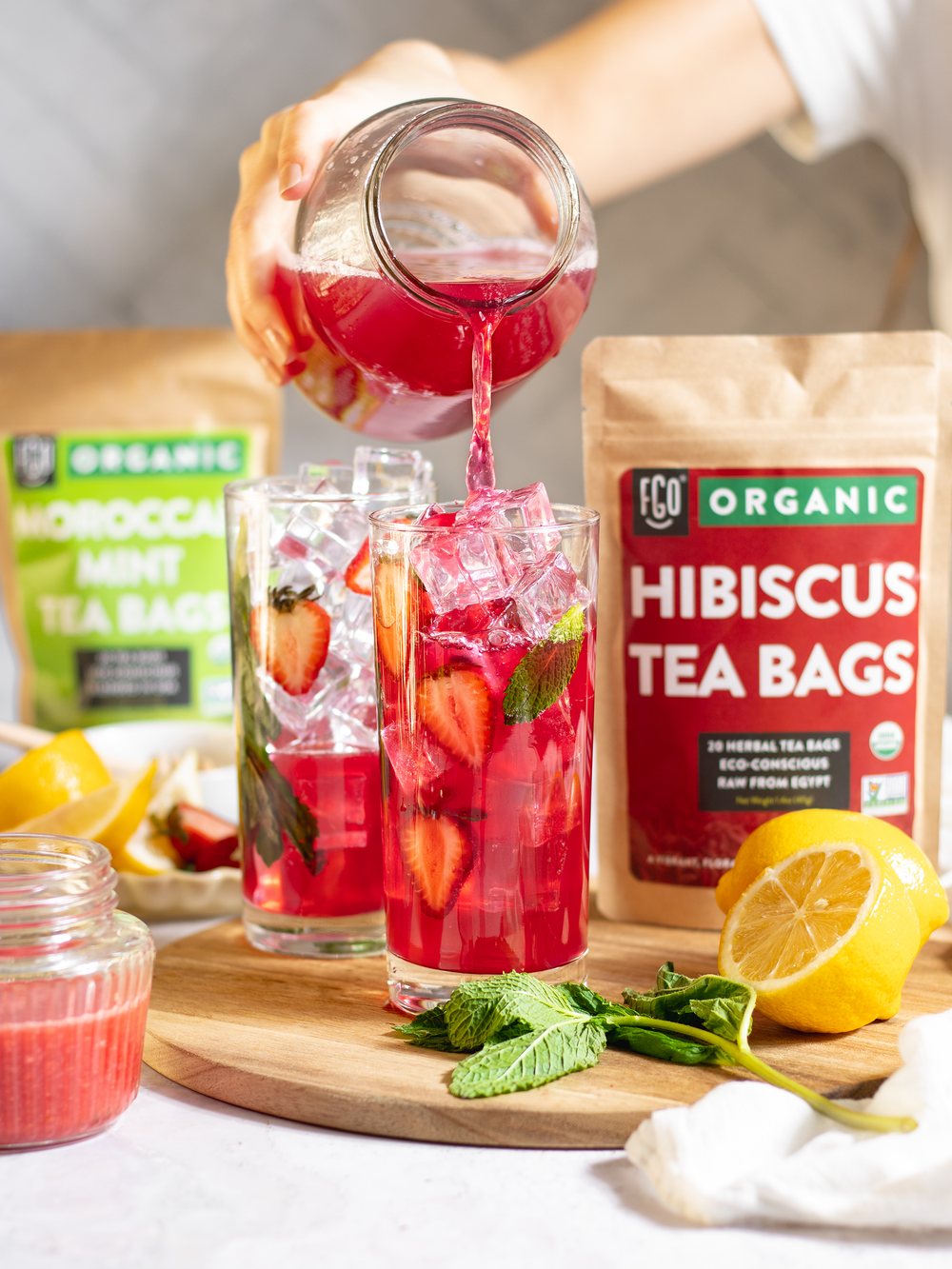 Hibiscus mint tea poured into a glass of ice with fresh strawberries and mint leaves.