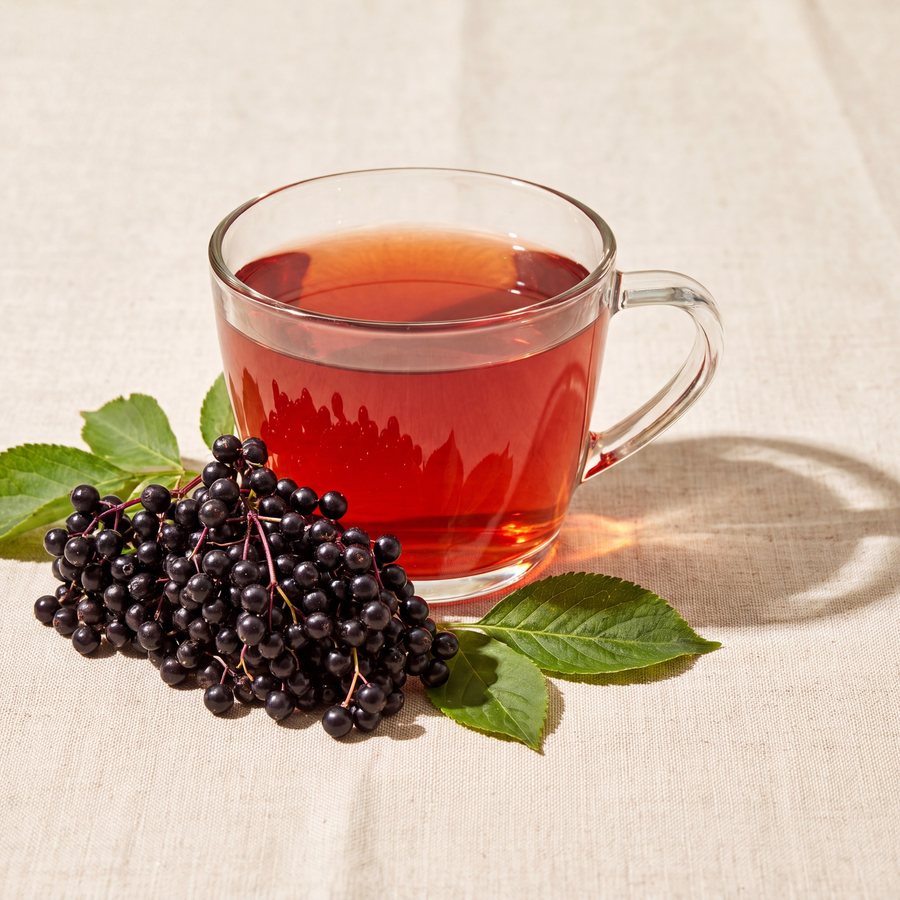 A glass cup of brewed elderberry tea, deep ruby-purple, beside the pouch