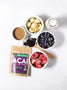 Ingredients for a frozen acai bowl including almond butter, frozen bananas, blueberries, strawberries, and almond milk.