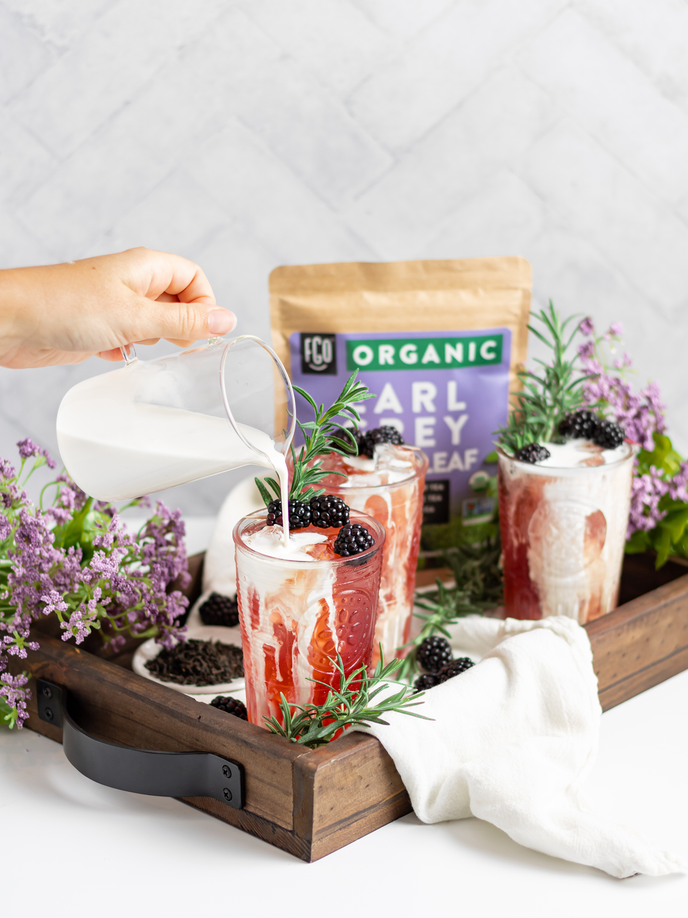 Milk poured over a glass of iced blackberry earl grey tea.