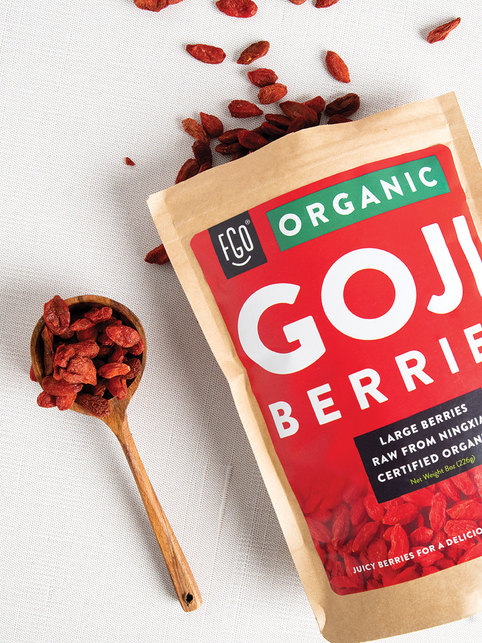 Raw goji berries in a wooden spoon spilled on the counter.