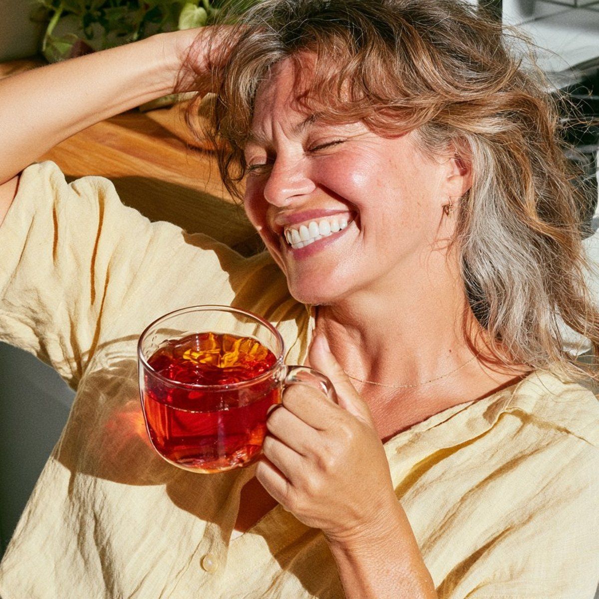 A woman in warm afternoon light holding a glass mug of brewed hibiscus tea