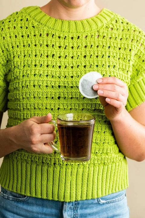 A mug of tea with an FGO tea bag, held in a knit sweater