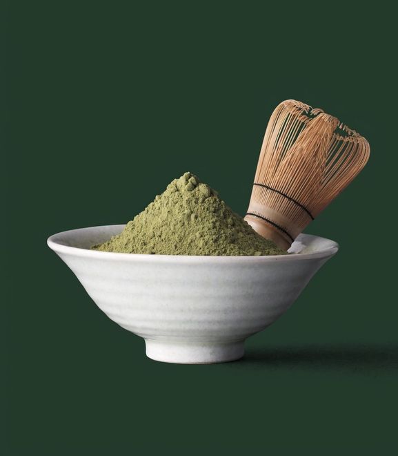 A bowl of matcha powder with a bamboo whisk on a deep green ground