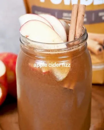 An apple cider fizz in a jar with apple slices and cinnamon sticks, in front of a pouch of Ceylon Cinnamon Powder