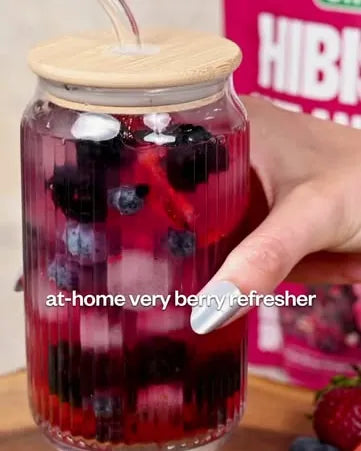 A jar glass of berry hibiscus refresher with blueberries and a straw, a pouch behind it