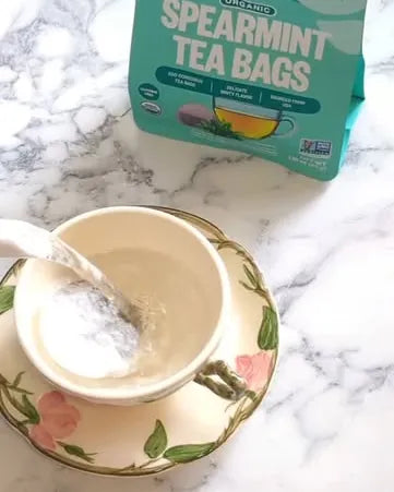 Hot water poured into a floral teacup beside a pouch of Spearmint Tea Bags
