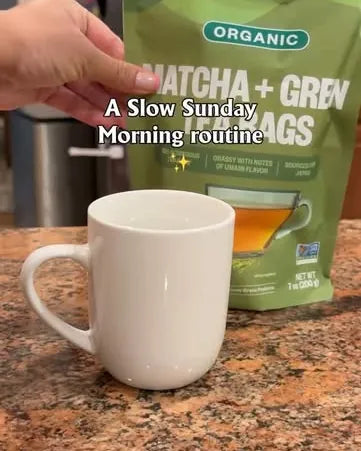 A white mug on a kitchen counter beside a pouch of Matcha + Green Tea Bags, with the words A slow Sunday morning routine