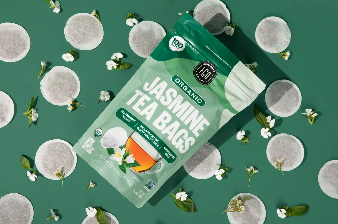 A Jasmine Tea Bags pack on a deep green backdrop with round tea bags and jasmine flowers