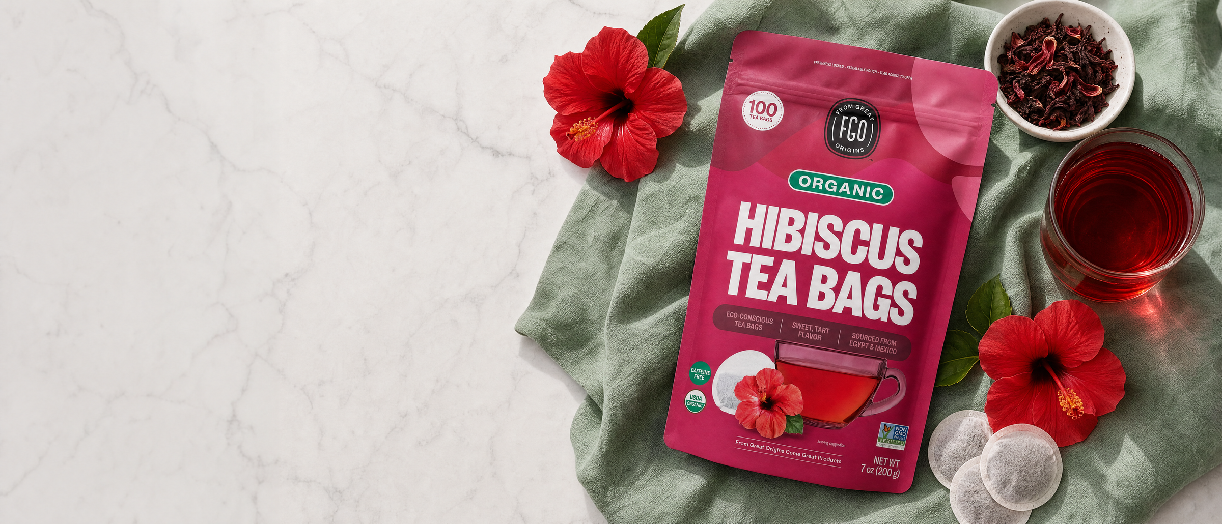 Organic Hibiscus Tea Bags on marble with fresh hibiscus flowers, brewed tea and round tea bags